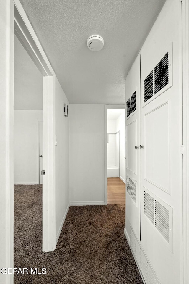 corridor with a textured ceiling and dark colored carpet