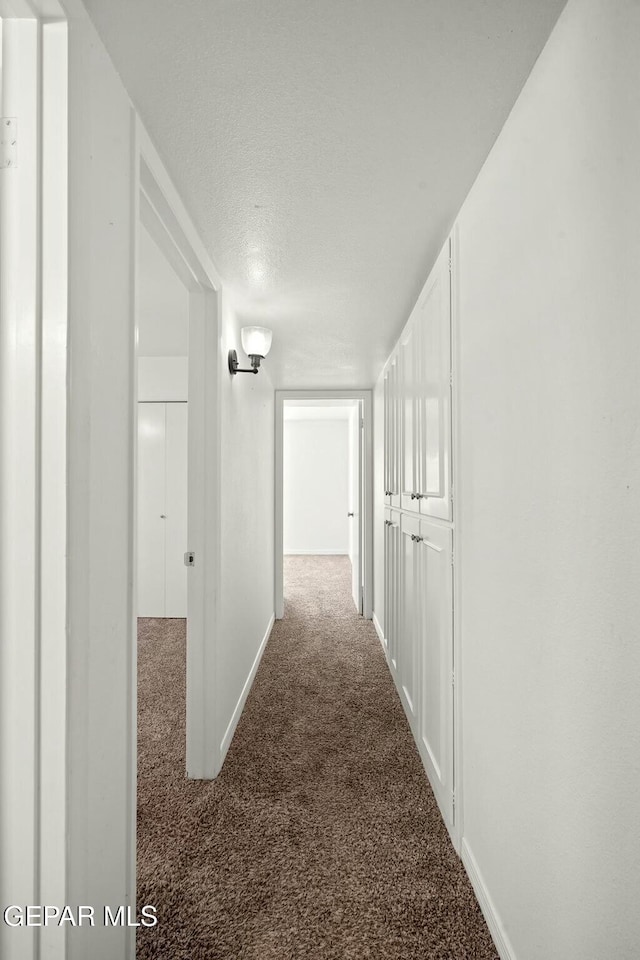 hall with a textured ceiling and dark colored carpet