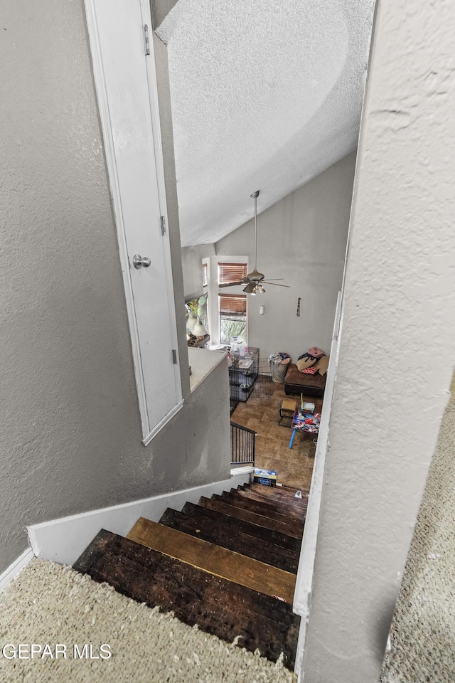 stairway featuring ceiling fan, lofted ceiling, and a textured ceiling