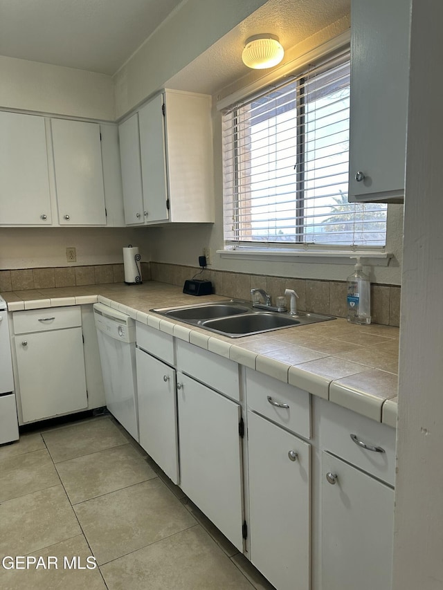 kitchen featuring dishwasher, sink, white cabinets, tile counters, and light tile patterned floors