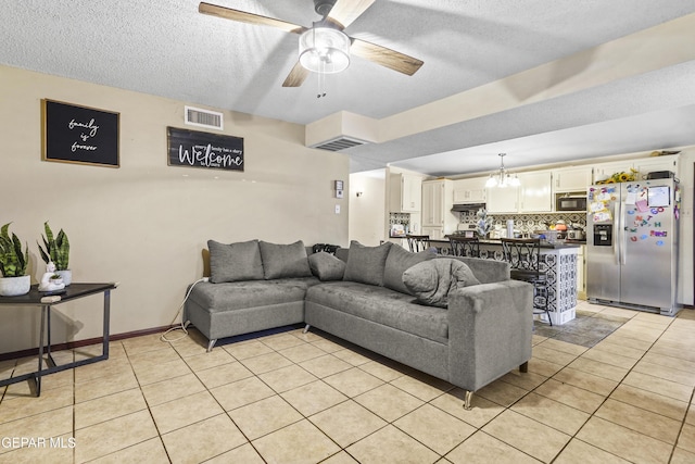 tiled living room with ceiling fan with notable chandelier and a textured ceiling