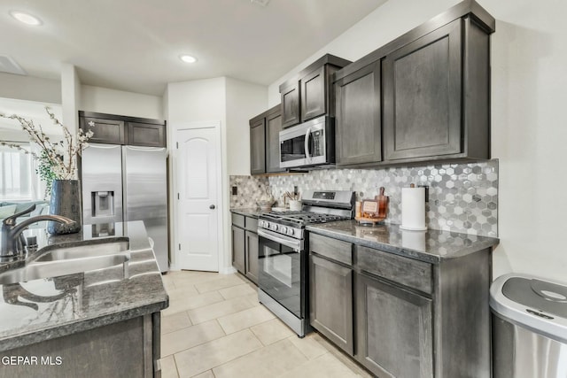 kitchen featuring stainless steel appliances, sink, dark brown cabinetry, and dark stone counters