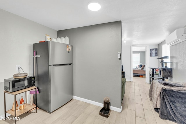 kitchen with stainless steel fridge, light hardwood / wood-style floors, and an AC wall unit