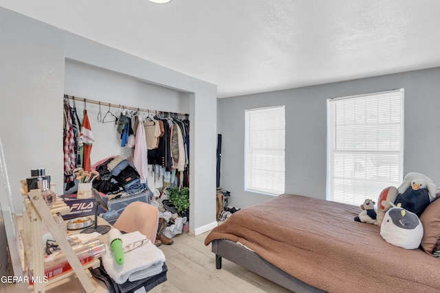 bedroom with multiple windows, a textured ceiling, light hardwood / wood-style floors, and a closet