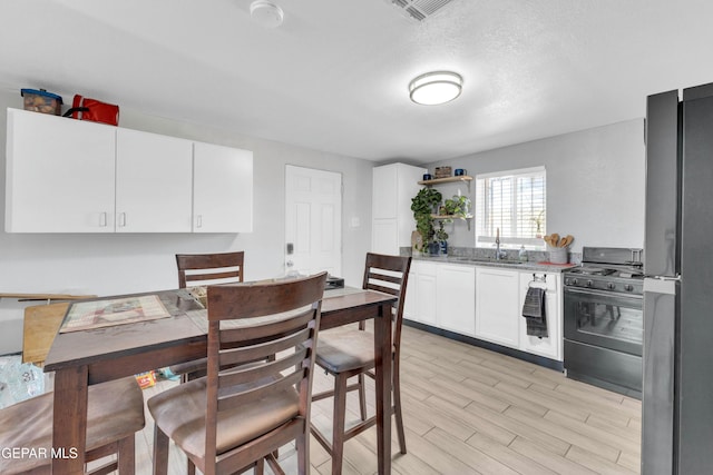 kitchen featuring refrigerator, white cabinetry, sink, gas stove, and light hardwood / wood-style flooring