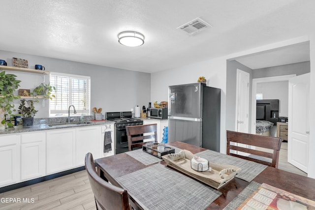 kitchen with sink, white cabinets, light stone counters, stainless steel appliances, and light hardwood / wood-style flooring