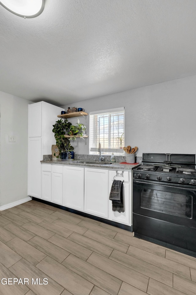 kitchen featuring sink, white cabinets, black range with gas stovetop, light stone countertops, and a textured ceiling