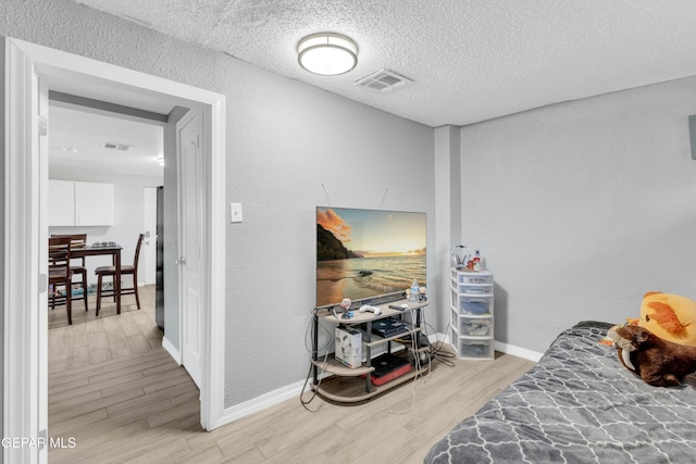 bedroom featuring stainless steel fridge, a textured ceiling, and light wood-type flooring