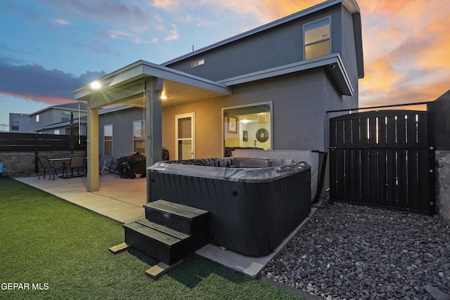 back house at dusk with a hot tub, a yard, and a patio area