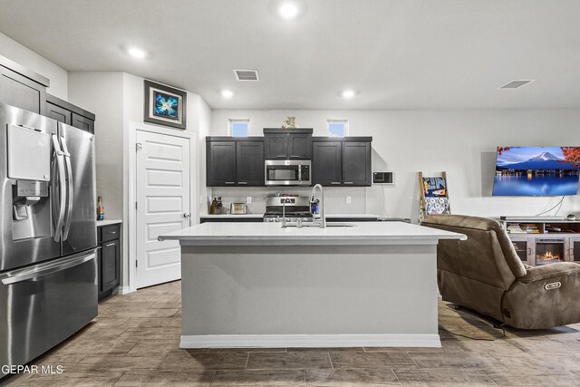 kitchen with stainless steel appliances, sink, a center island with sink, and backsplash