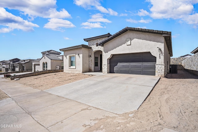 mediterranean / spanish-style house featuring stucco siding, an attached garage, central AC, stone siding, and driveway