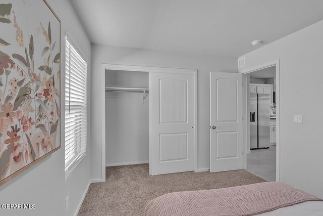 carpeted bedroom with stainless steel refrigerator with ice dispenser and a closet