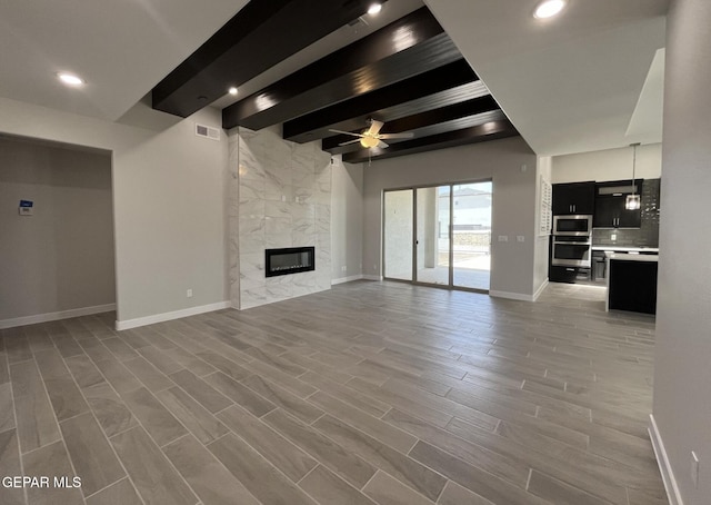 unfurnished living room featuring wood-type flooring, a fireplace, beamed ceiling, and ceiling fan