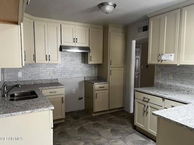 kitchen with cream cabinets, backsplash, light stone countertops, and sink