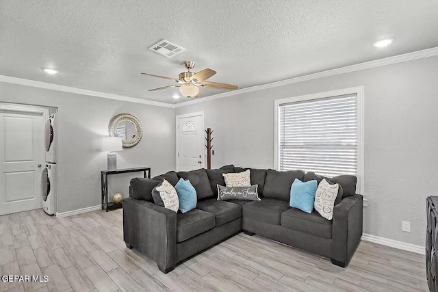 living room featuring stacked washer and clothes dryer, crown molding, a textured ceiling, ceiling fan, and light hardwood / wood-style floors