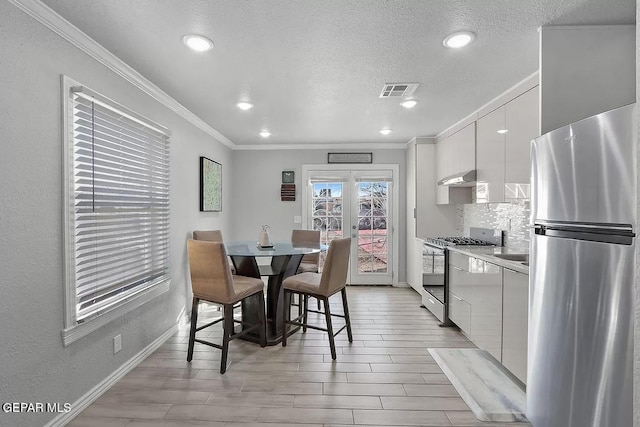 kitchen featuring crown molding, appliances with stainless steel finishes, white cabinets, decorative backsplash, and french doors