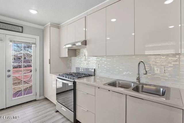 kitchen with sink, gas stove, tasteful backsplash, ornamental molding, and white cabinets