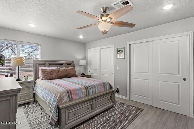 bedroom featuring ceiling fan, a textured ceiling, multiple closets, and light wood-type flooring