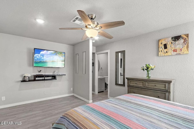 bedroom featuring ceiling fan, hardwood / wood-style floors, a textured ceiling, and ensuite bath