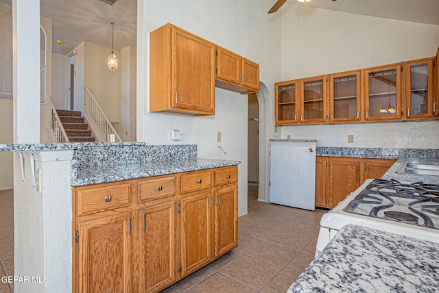 kitchen featuring gas range gas stove, decorative light fixtures, light tile patterned floors, ceiling fan, and light stone countertops