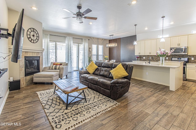 living room with a tile fireplace, dark wood-type flooring, sink, and ceiling fan