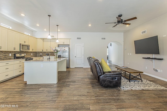 kitchen with sink, appliances with stainless steel finishes, light stone counters, a center island with sink, and decorative light fixtures