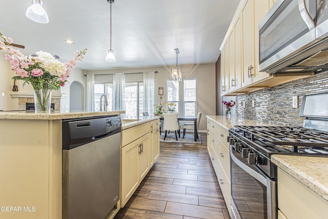 kitchen featuring pendant lighting, appliances with stainless steel finishes, cream cabinets, and backsplash