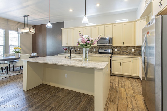 kitchen with sink, decorative light fixtures, appliances with stainless steel finishes, an island with sink, and light stone countertops