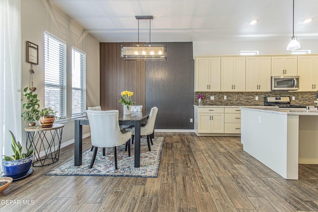 kitchen featuring decorative light fixtures, wood-type flooring, stainless steel appliances, light stone countertops, and cream cabinetry