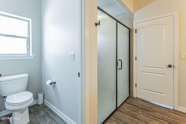 bathroom with wood-type flooring, a shower with shower door, and toilet