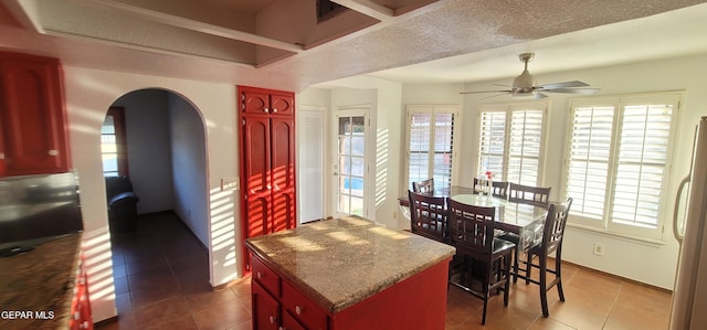 kitchen featuring ceiling fan, tile patterned flooring, fridge, a center island, and a textured ceiling