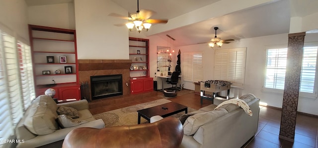 living room featuring a tiled fireplace, vaulted ceiling, dark tile patterned floors, and ceiling fan