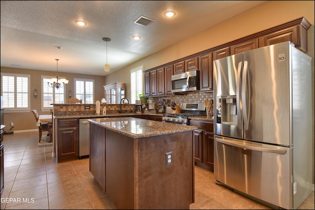 kitchen featuring appliances with stainless steel finishes, hanging light fixtures, a center island, kitchen peninsula, and dark brown cabinets