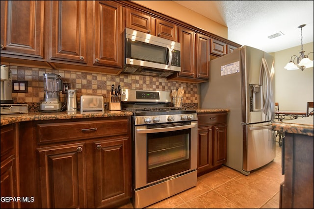 kitchen with tasteful backsplash, hanging light fixtures, light tile patterned floors, dark stone countertops, and appliances with stainless steel finishes