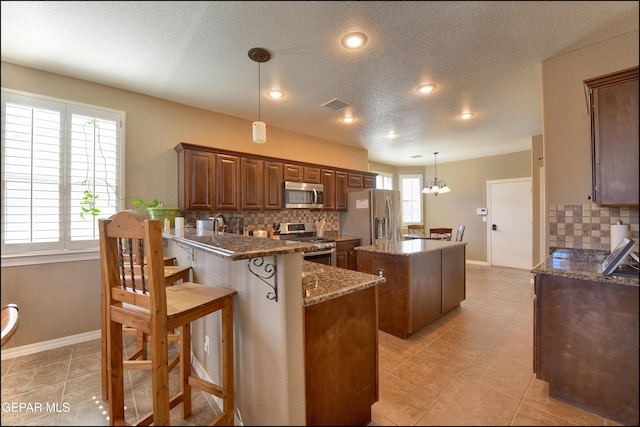 kitchen featuring a kitchen island, appliances with stainless steel finishes, pendant lighting, dark stone countertops, and backsplash