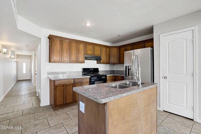 kitchen featuring sink, light tile patterned floors, stainless steel refrigerator with ice dispenser, a center island with sink, and black gas range