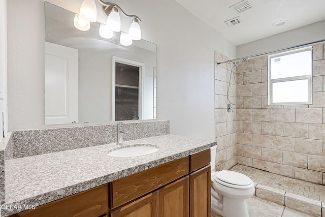 bathroom featuring vanity, a tile shower, tile patterned floors, and toilet