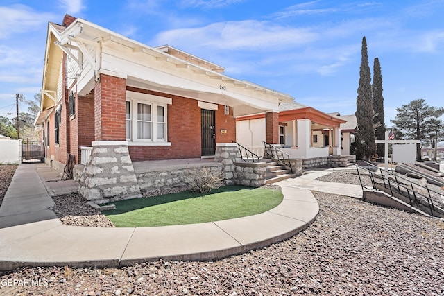 view of front of house with covered porch, brick siding, fence, and a gate