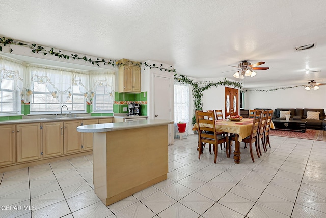 kitchen featuring sink, light tile patterned floors, ceiling fan, a center island, and a textured ceiling