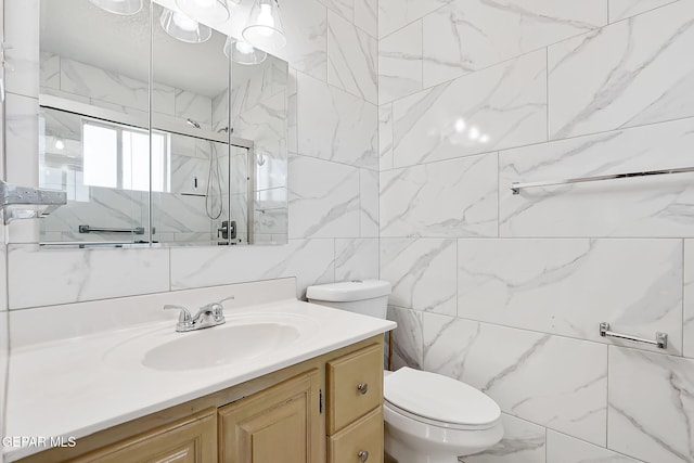 bathroom with vanity, a shower with door, tile walls, and toilet