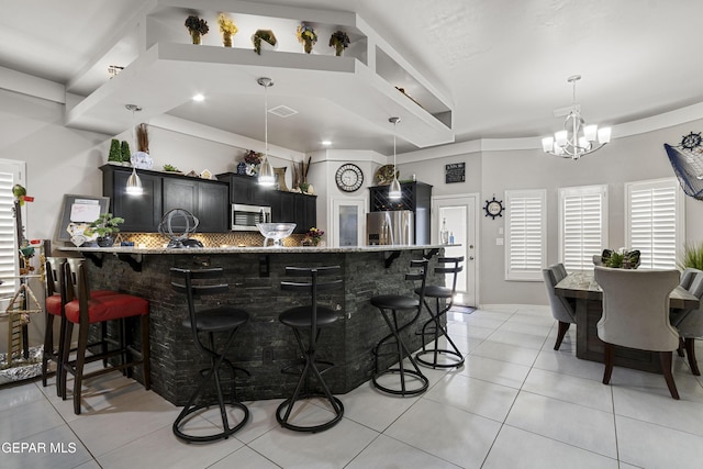 kitchen with light tile patterned flooring, appliances with stainless steel finishes, a kitchen breakfast bar, hanging light fixtures, and a notable chandelier