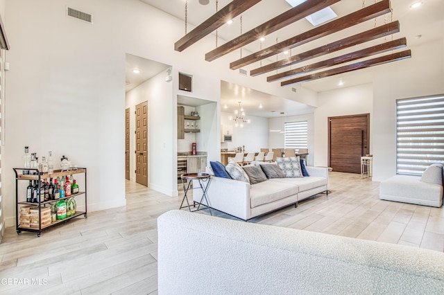 living room with beamed ceiling, a chandelier, light hardwood / wood-style floors, and a high ceiling