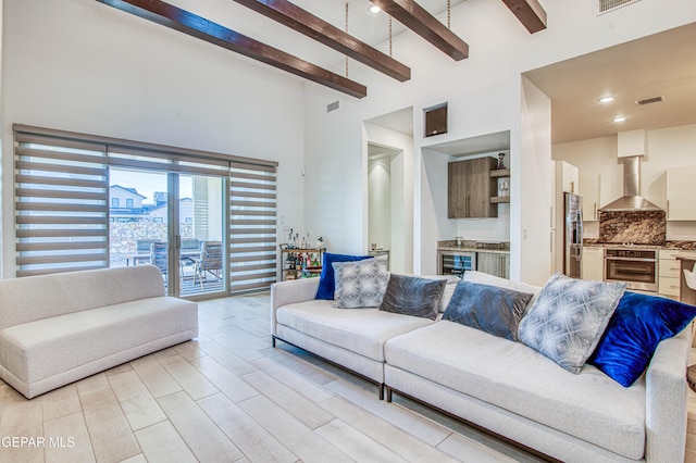 living room with beam ceiling, light wood-type flooring, a towering ceiling, and indoor bar