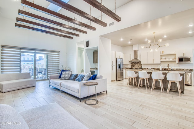 living room featuring sink, light hardwood / wood-style flooring, a chandelier, a high ceiling, and beamed ceiling