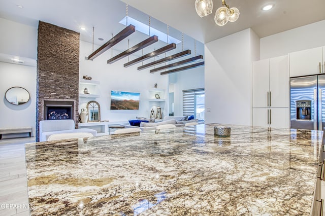 kitchen with a fireplace, white cabinets, a high ceiling, light stone counters, and light hardwood / wood-style flooring