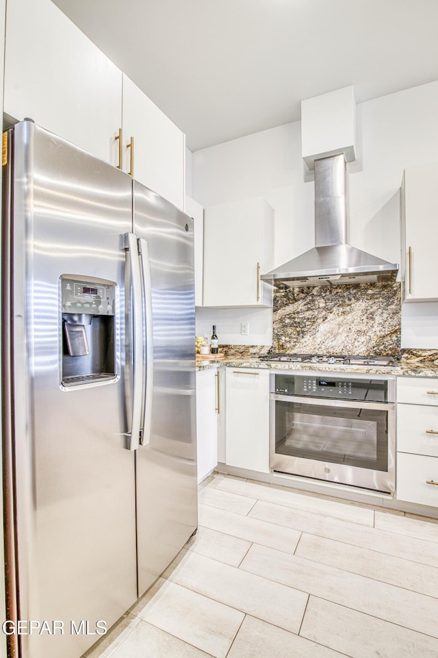 kitchen with dark stone countertops, stainless steel appliances, wall chimney exhaust hood, and white cabinets