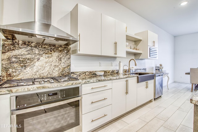 kitchen with appliances with stainless steel finishes, sink, white cabinets, decorative backsplash, and wall chimney range hood