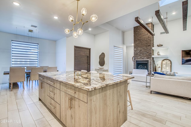 kitchen with a stone fireplace, a center island, light stone counters, light hardwood / wood-style floors, and light brown cabinets