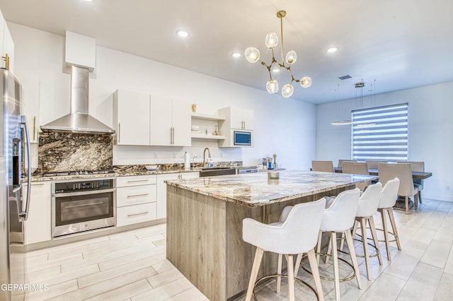 kitchen featuring a kitchen island, white cabinets, pendant lighting, stainless steel appliances, and wall chimney range hood