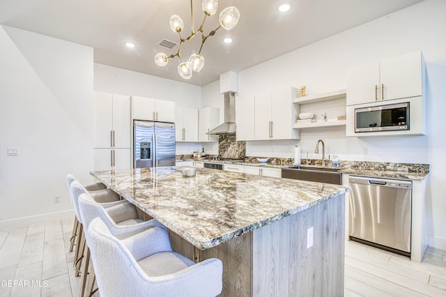 kitchen featuring wall chimney range hood, sink, stainless steel appliances, a center island, and white cabinets